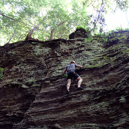 man climbing up rock face in harness